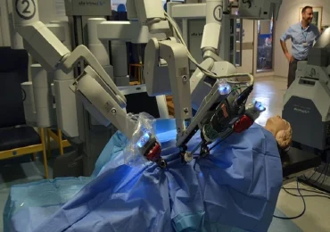 Un robot chirurgico da Vinci in funzione, con bracci meccanici illuminati che operano su un manichino in un ambiente ospedaliero.