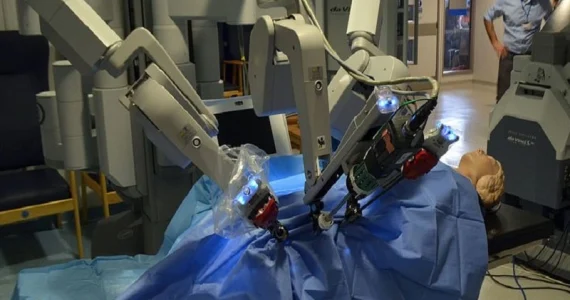 Un robot chirurgico da Vinci in funzione, con bracci meccanici illuminati che operano su un manichino in un ambiente ospedaliero.